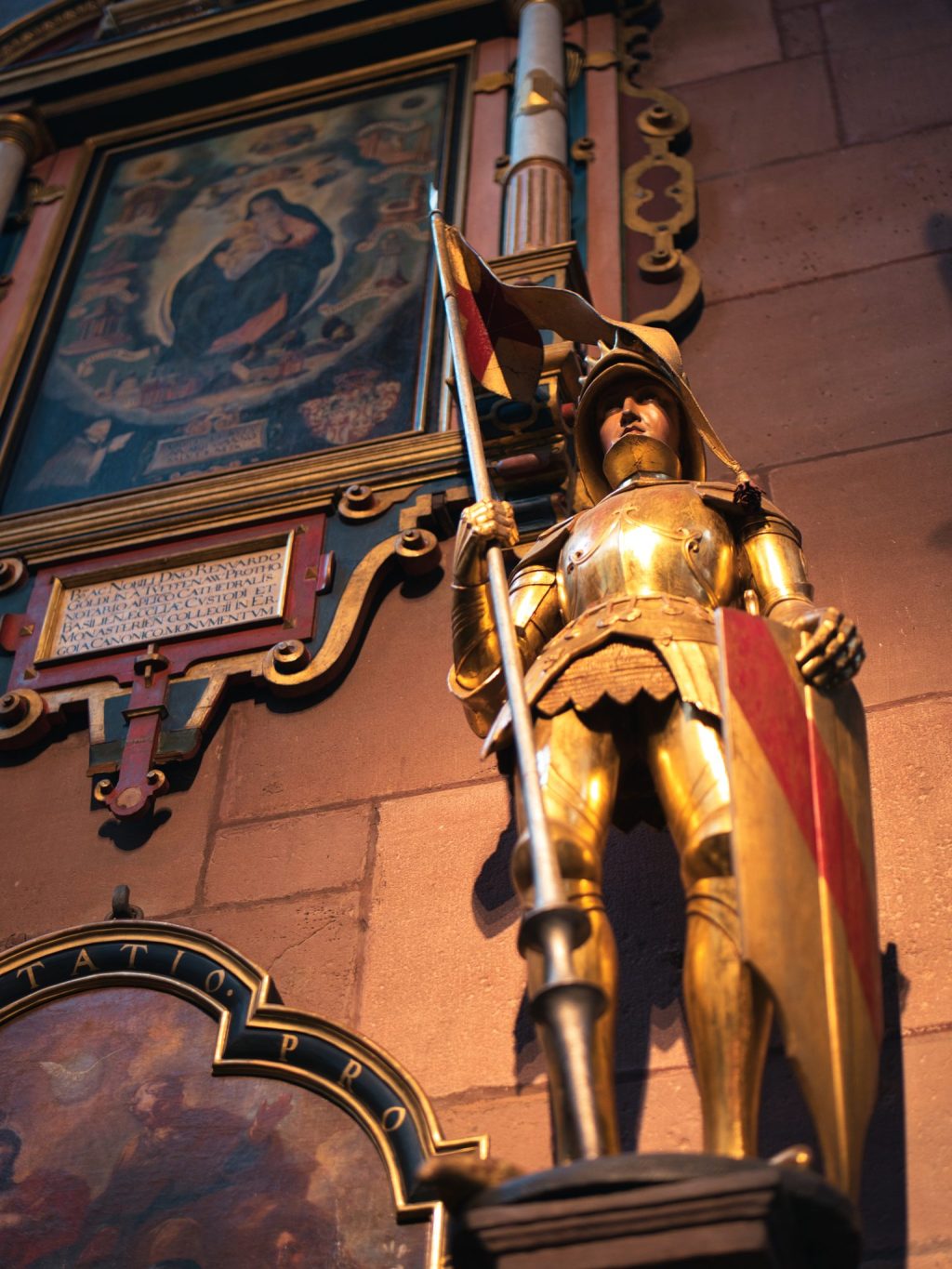 Statue d'un chevalier en armure dorée tenant une lance et un écu, devant un tableau de la Vierge, dans la cathédrale de Fribourg-en-Brisgau