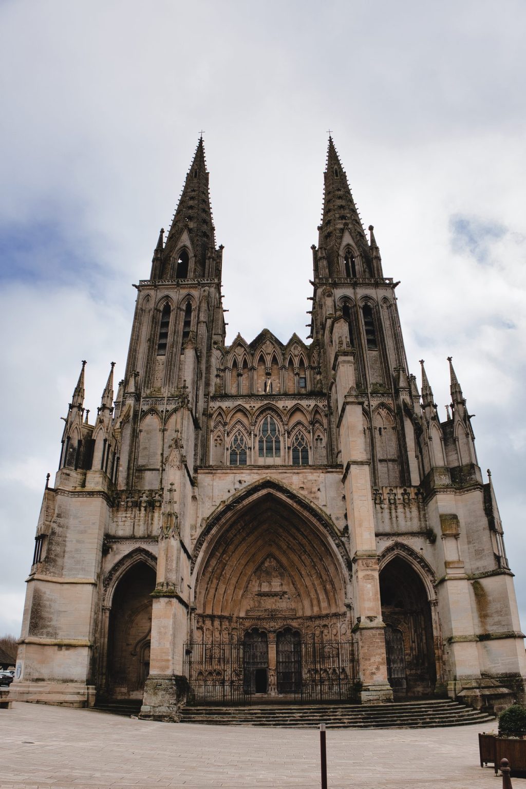 Façade occidentale et flèches gothiques de la cathédrale Notre-Dame de Sées, dans l'Orne, sous un ciel nuageux