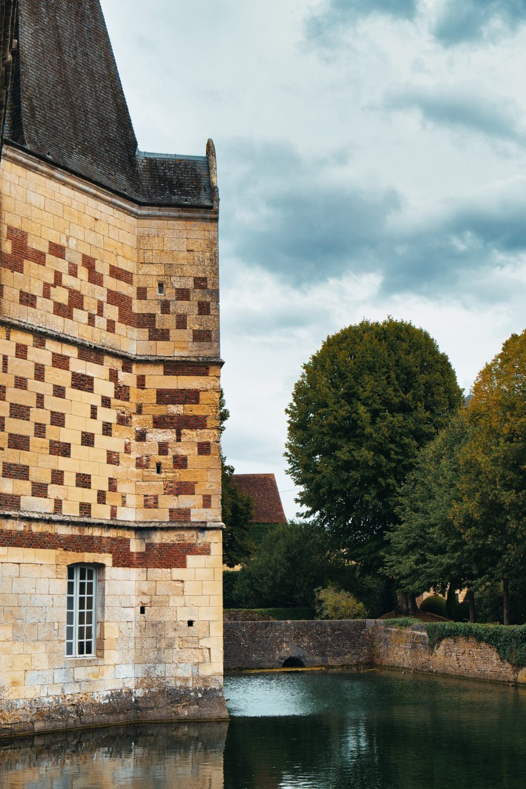 Mur de brique et de pierre en damier du château d'Ô se reflétant dans les douves, à Mortrée dans l'Orne