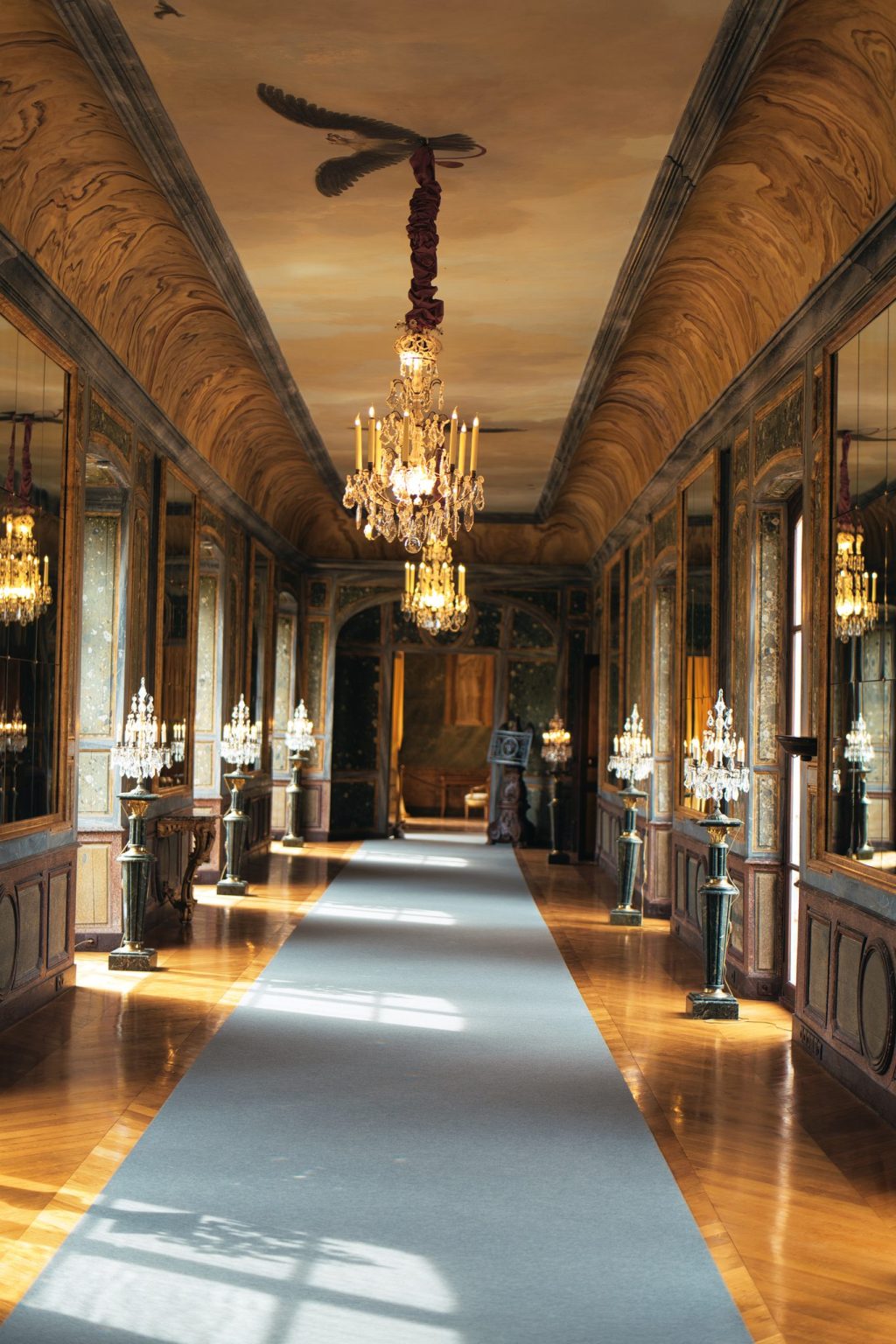 Galerie éclairée de lustres en cristal, de miroirs et de torchères, au château d'Ô dans l'Orne