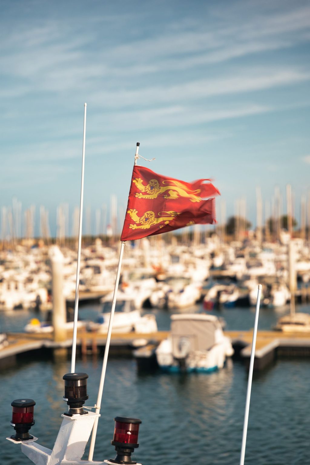 Drapeau normand rouge aux deux léopards d'or flottant à la proue d'un bateau, devant les voiliers d'un port du Cotentin