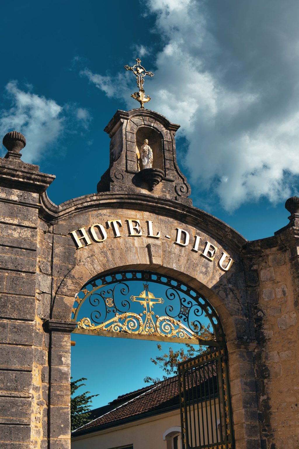 Portail en pierre de l'Hôtel-Dieu de Sées surmonté d'une niche avec statue et d'une croix, avec sa grille dorée