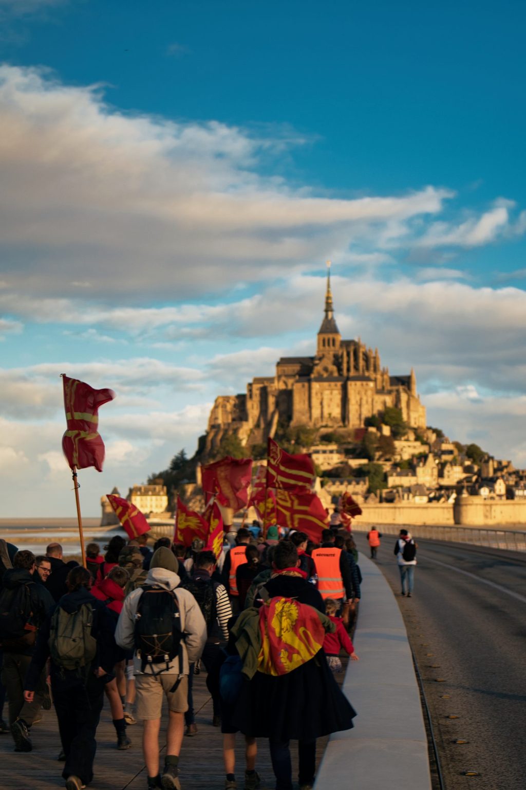 Pèlerins portant des drapeaux rouges et or sur la passerelle menant au Mont-Saint-Michel, dans la lumière du matin