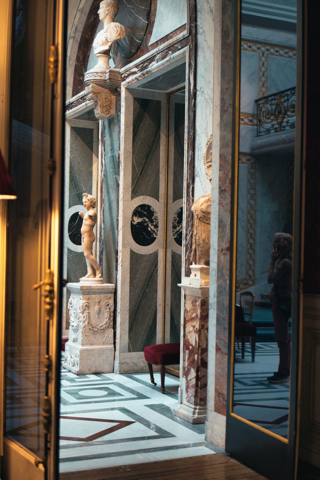 Porte vitrée ouvrant sur une salle de marbres polychromes, une statue et un buste, au musée Jacquemart-André à Paris